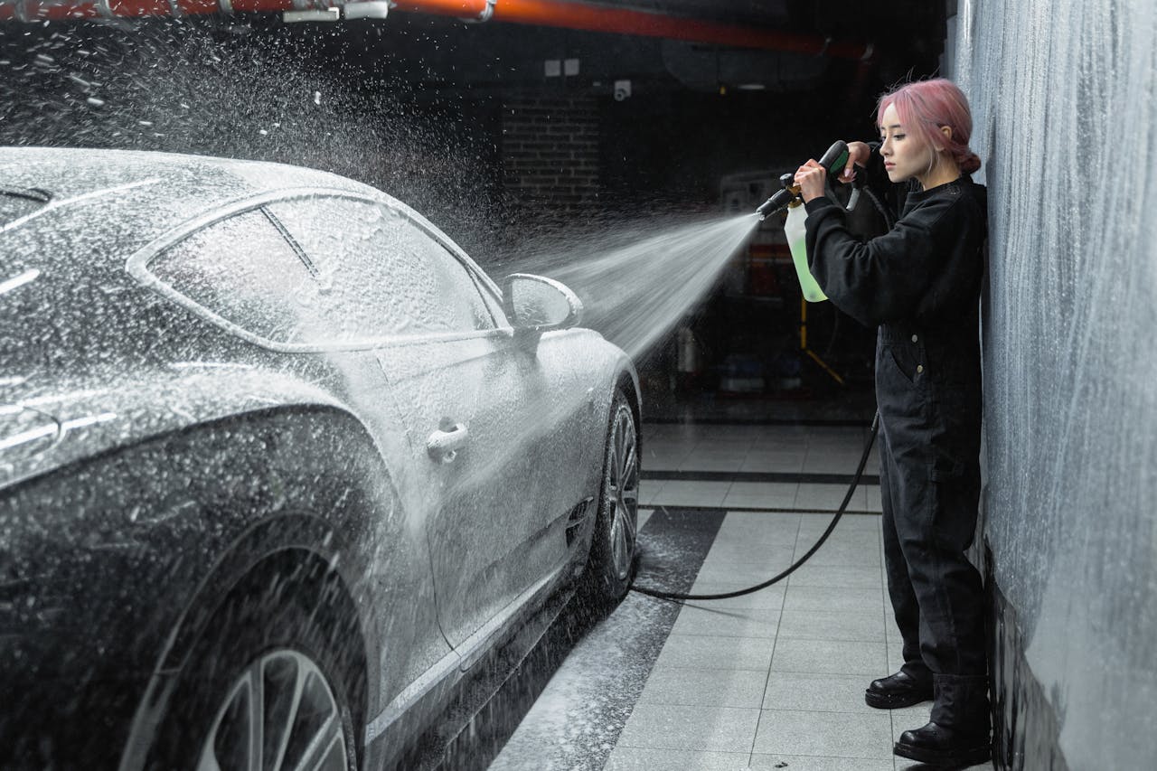 hero-img An Asian woman using a pressure washer to clean a car at an indoor car wash facility.